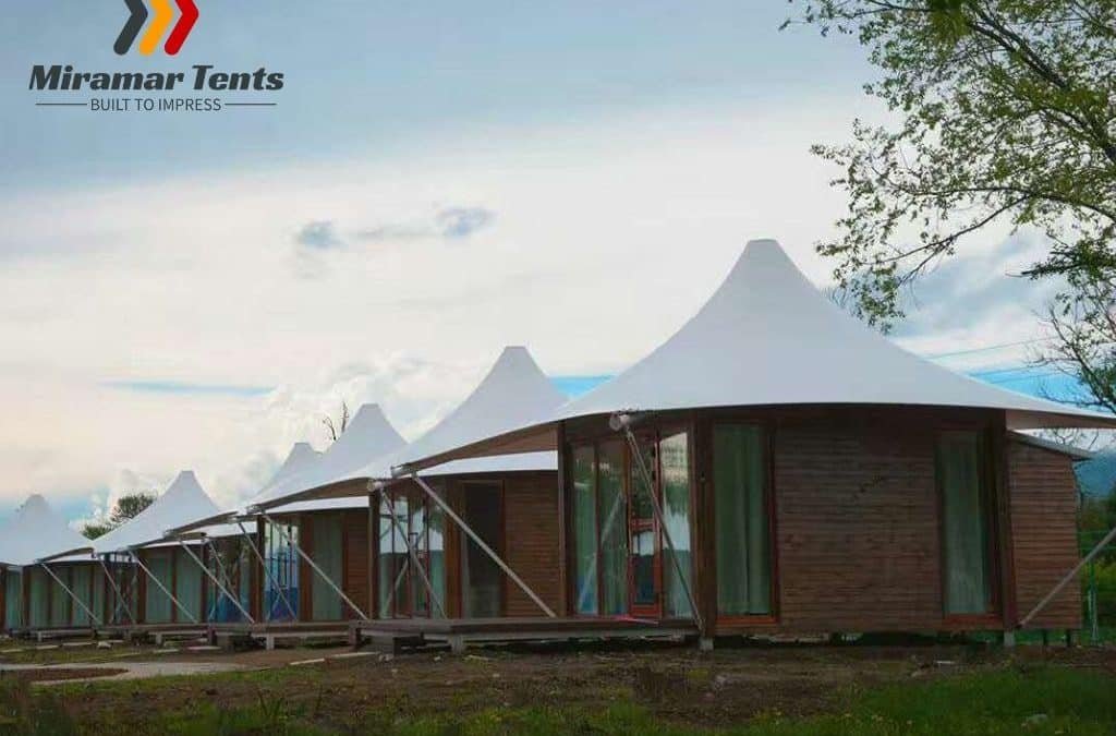 Row of modern wooden glamping tents with white peaked roofs in a scenic outdoor setting.