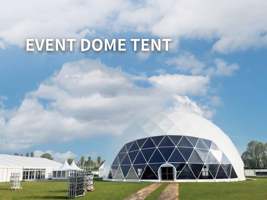 A large geodesic dome tent is set up on a grass field under a partly cloudy sky, with a few smaller tents visible in the background.