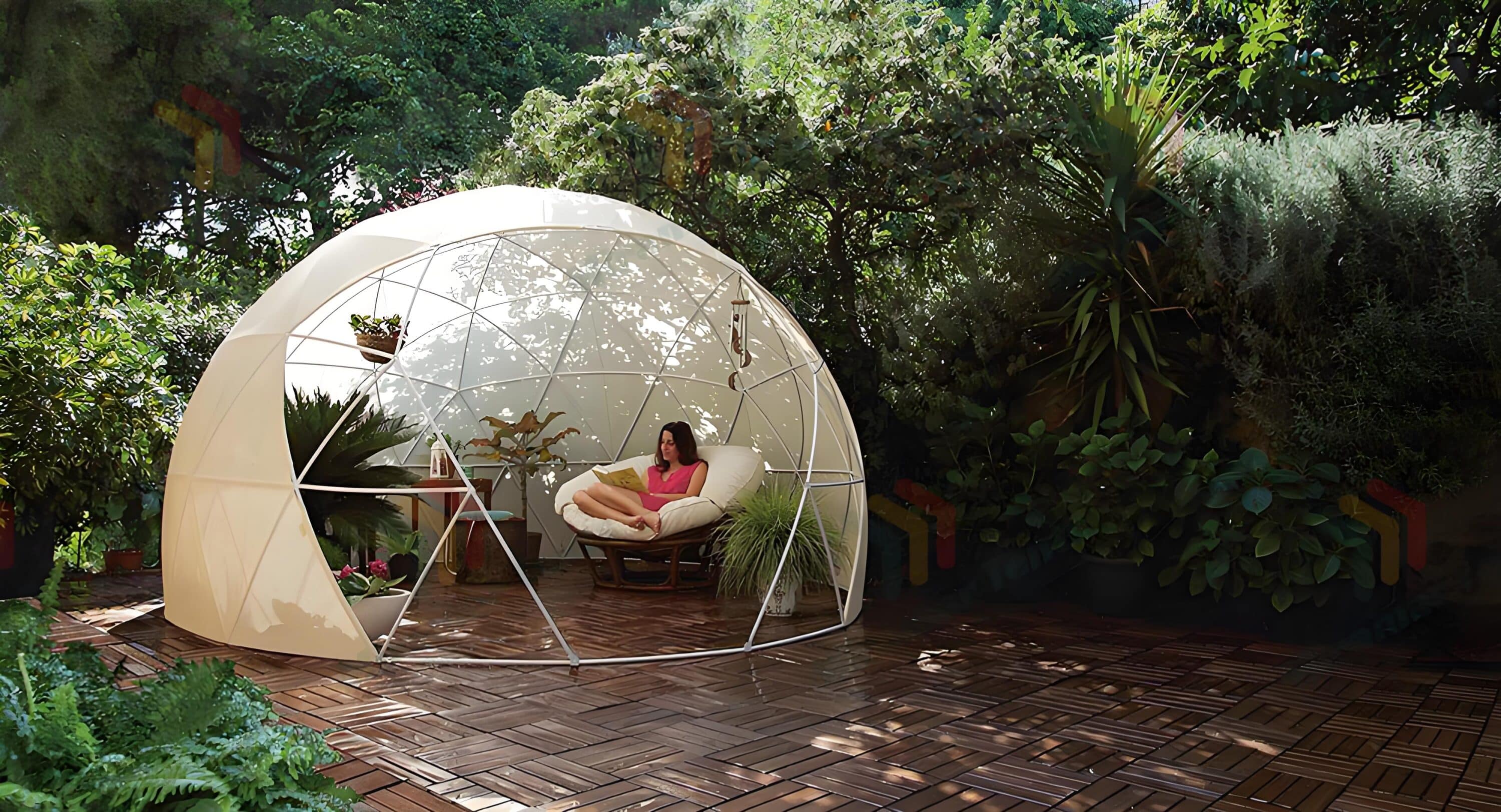 A person sits on a cushioned chair inside a geodesic dome structure in a lush garden.