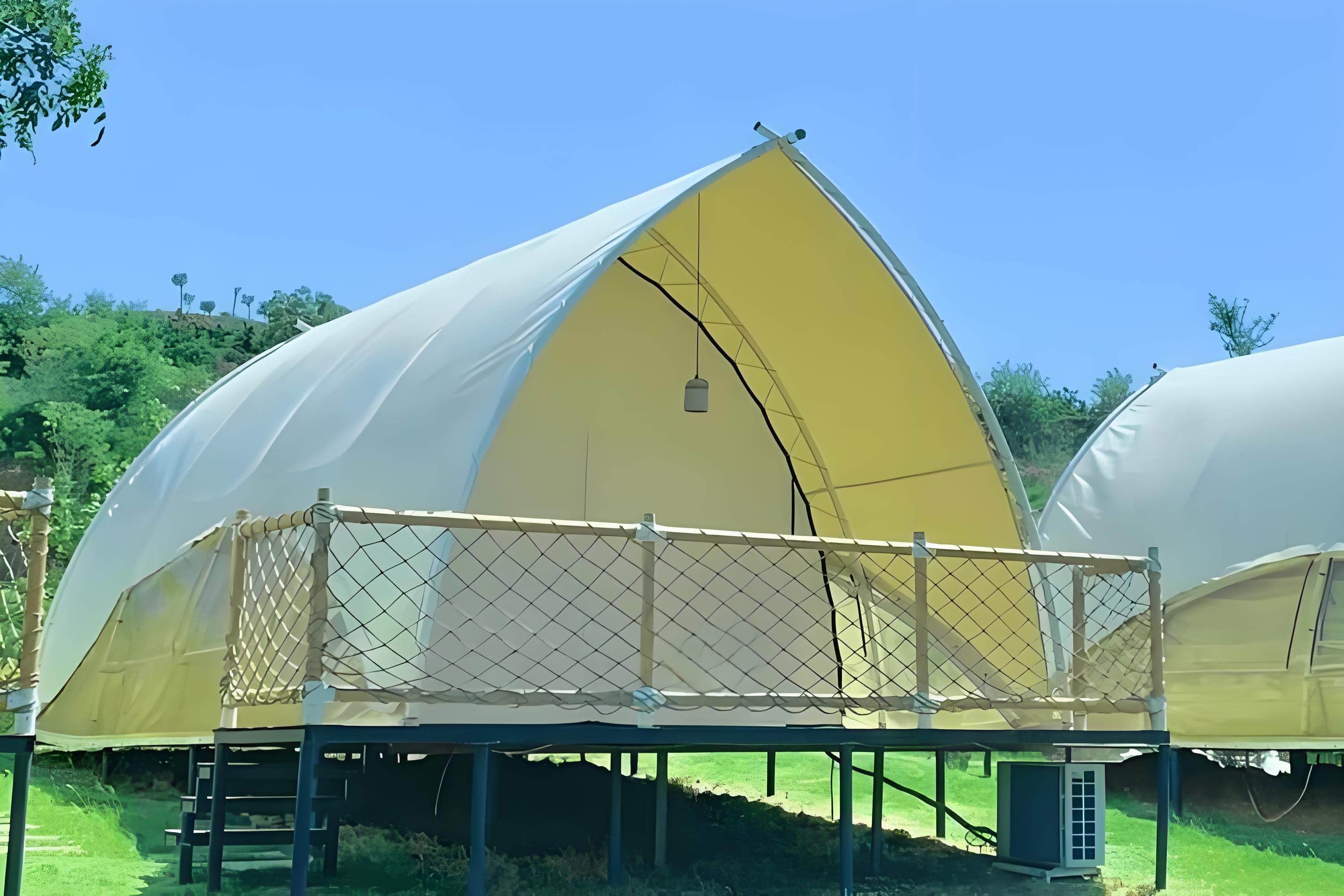 A covered wagon with a white canvas top is parked on a grassy hill, surrounded by trees and foliage. Steps lead up to a door at the rear of the wagon.