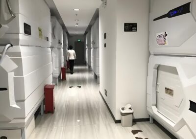 A Person Walks Down A Hallway Lined With Futuristic Sleeping Pods.