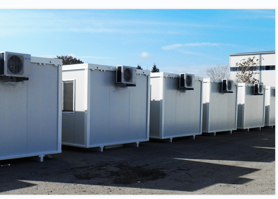 A row of sleek white foldable container houses with air conditioning units, set on a paved surface under a clear blue sky.