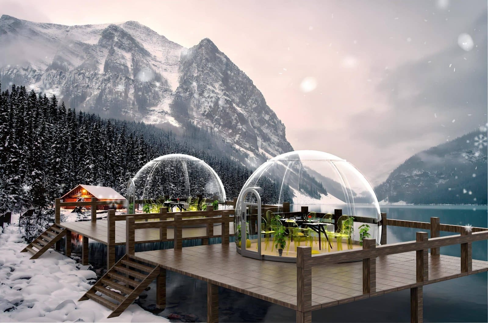 Snow-covered wooden deck on a lake, featuring two clear dining domes with tables and chairs, surrounded by snowy mountains and pine trees in the background.