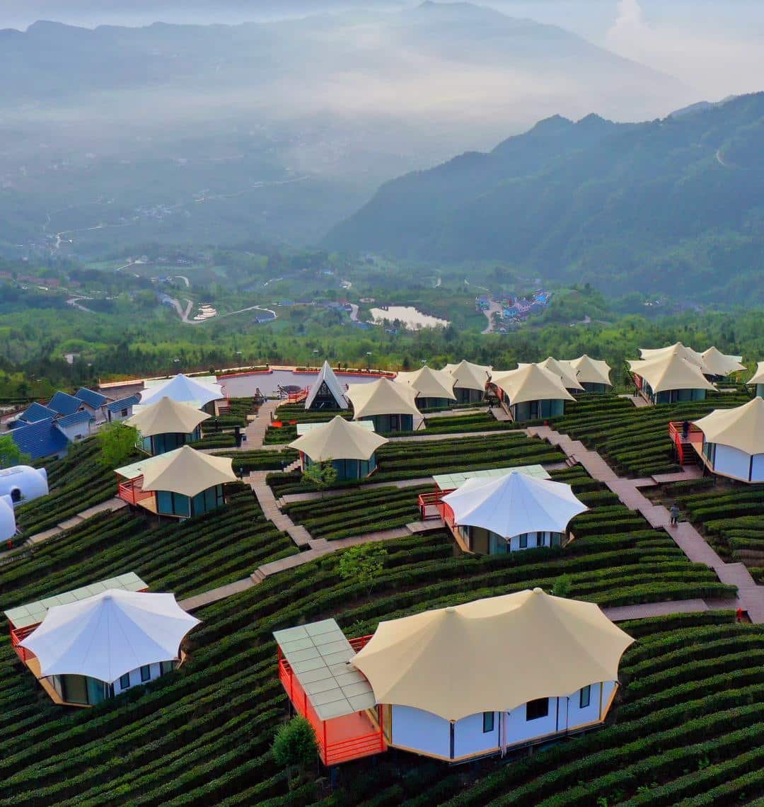 Aerial view of glamping tents arranged on terraced hillsides with mountains and mist in the background.